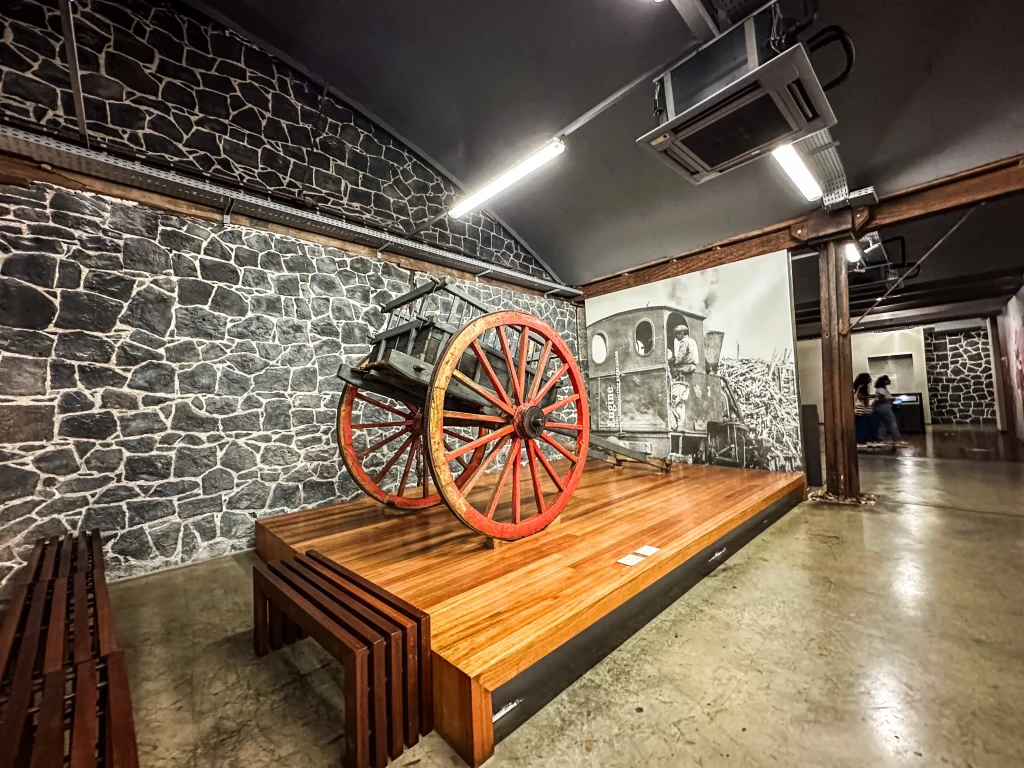 A vintage wooden cart and historical photo exhibit in a Mauritian museum, showcasing what to do in Port Louis for history buffs