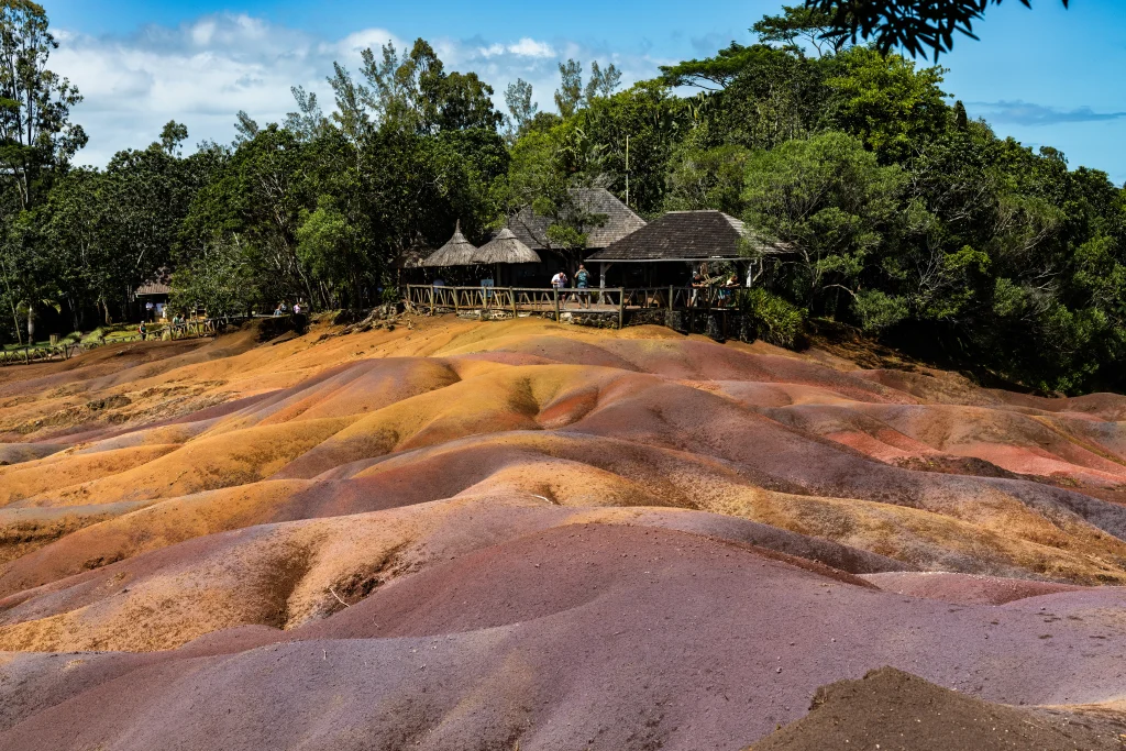 Rolling dunes of multi-colored volcanic earth in shades of red and brown, bordered by a wooden fence and a stone-paved path
