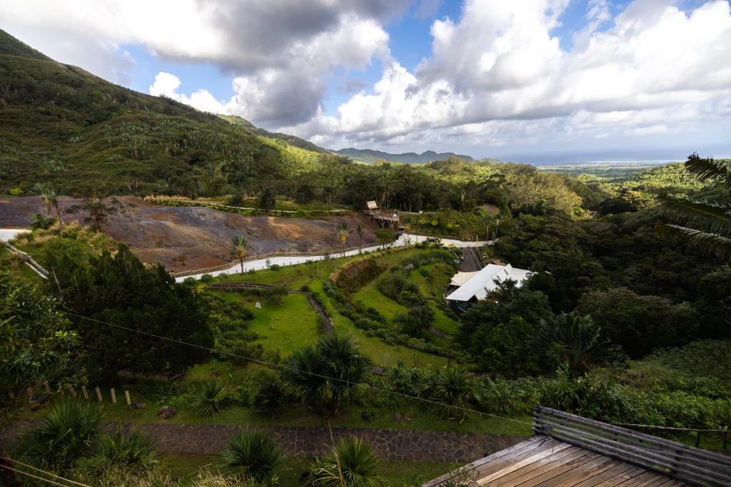 A high-angle view of a lush green valley with winding paths and a white-roofed building, showing the volcanic landscapes of Mauritius