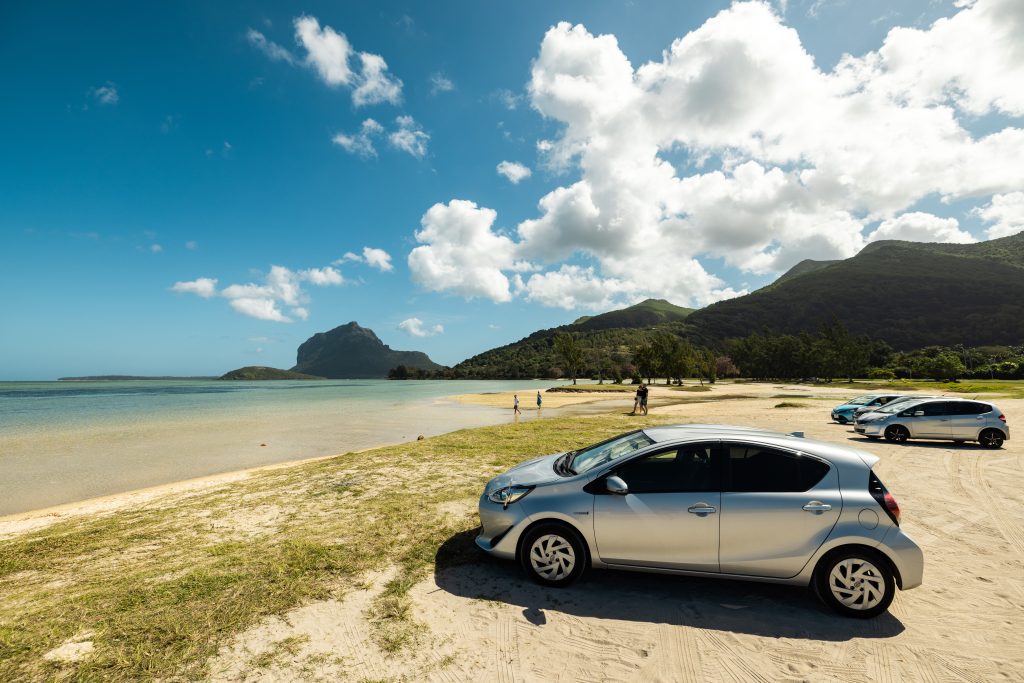 Rental car parked on a tropical beach in Mauritius with turquoise water, mountains, and clear blue skies